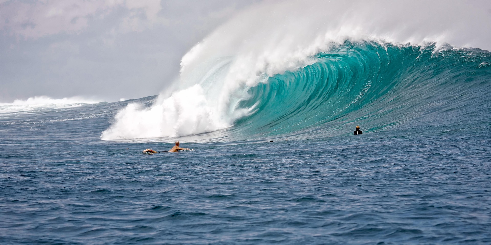 Surfers paddling toward a massive breaking wave